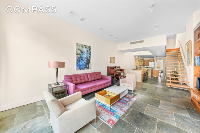 living area featuring visible vents, baseboards, stone finish flooring, and stairway