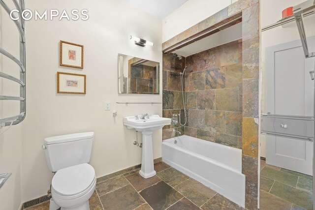 full bathroom with baseboards, stone tile flooring,  shower combination, and toilet