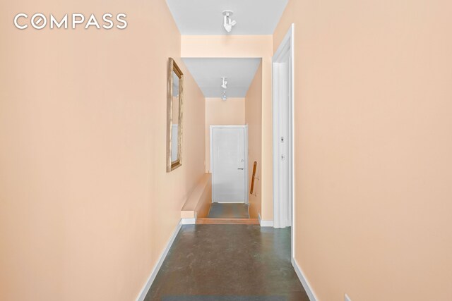 hall featuring finished concrete floors, baseboards, and an upstairs landing