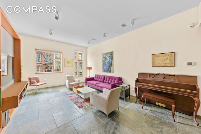 living area featuring baseboards, stone finish floor, and visible vents
