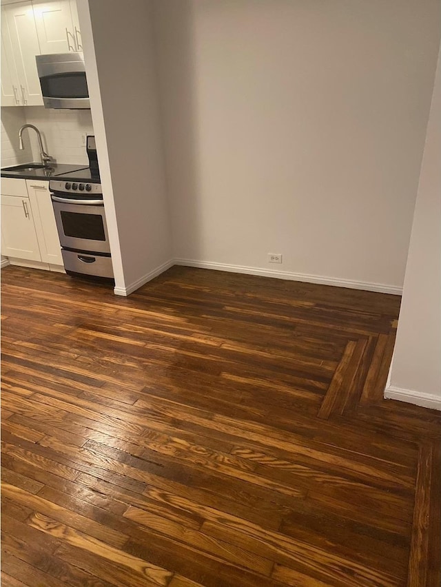 unfurnished dining area featuring baseboards, dark wood-style flooring, and a sink