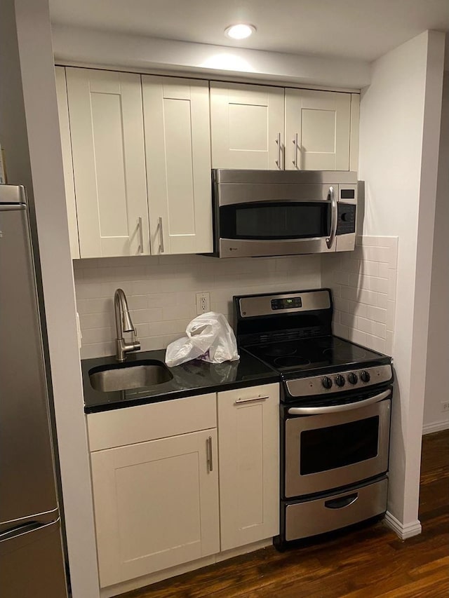 kitchen featuring dark wood-style floors, a sink, dark countertops, backsplash, and appliances with stainless steel finishes