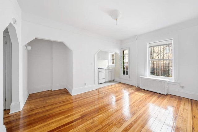 315 W 71st St, New York City, NY 10023 - unfurnished living room with radiator heating unit, light wood-type flooring, and arched walkways