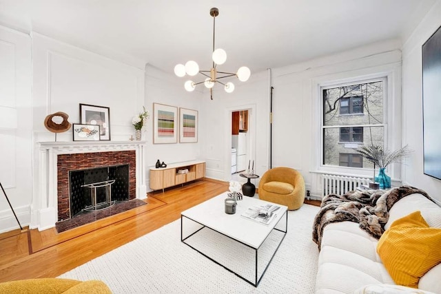 315 W 71st St, New York City, NY 10023 - living room featuring light wood-type flooring, a chandelier, radiator heating unit, and a brick fireplace