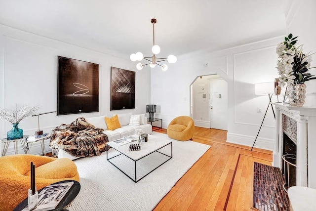 315 W 71st St, New York City, NY 10023 - living area with light wood-type flooring, a chandelier, a fireplace with flush hearth, arched walkways, and baseboards