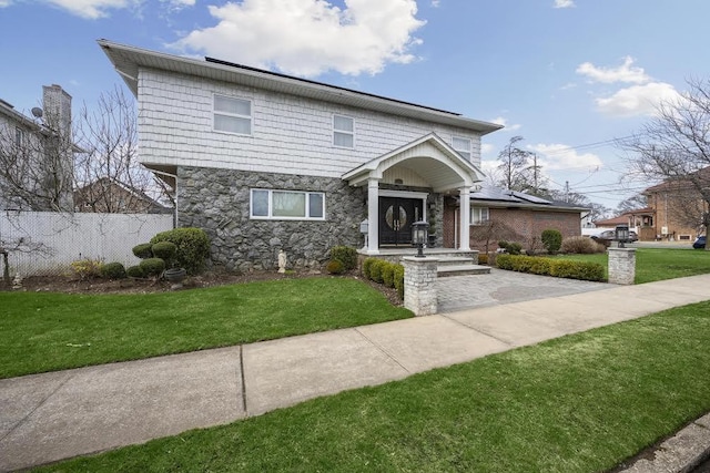 view of front facade featuring a front lawn, fence, stone siding, and roof mounted solar panels
