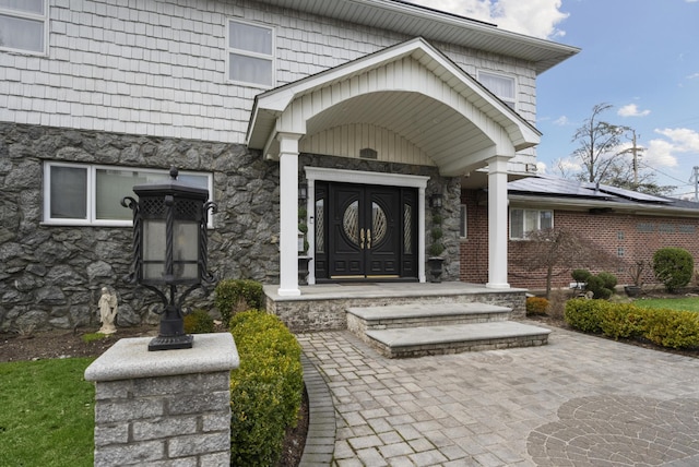entrance to property featuring roof mounted solar panels and stone siding