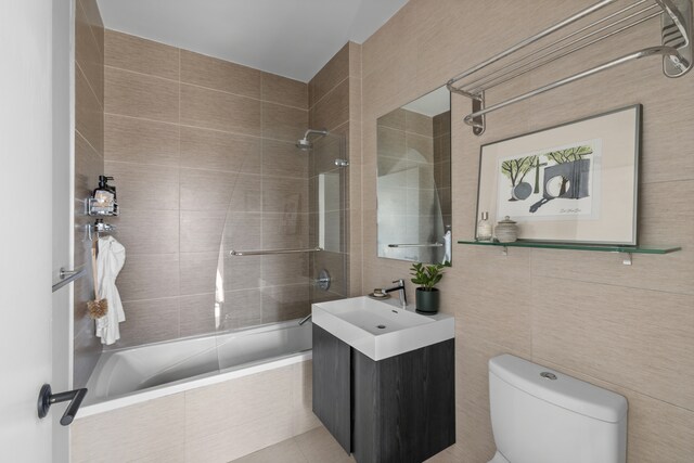 bathroom with tiled shower / bath combo, toilet, tile walls, and vanity