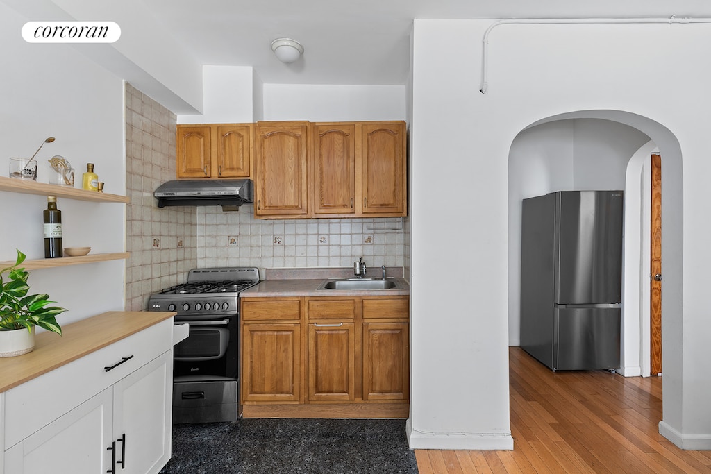 240 E 24th St Unit 1E, New York City, NY 10010 - kitchen with freestanding refrigerator, range with gas cooktop, under cabinet range hood, open shelves, and tasteful backsplash