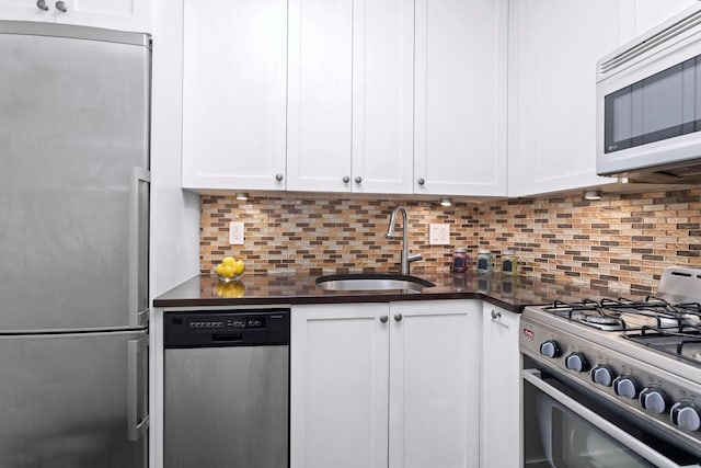 kitchen with white cabinets, a sink, dark countertops, stainless steel appliances, and decorative backsplash