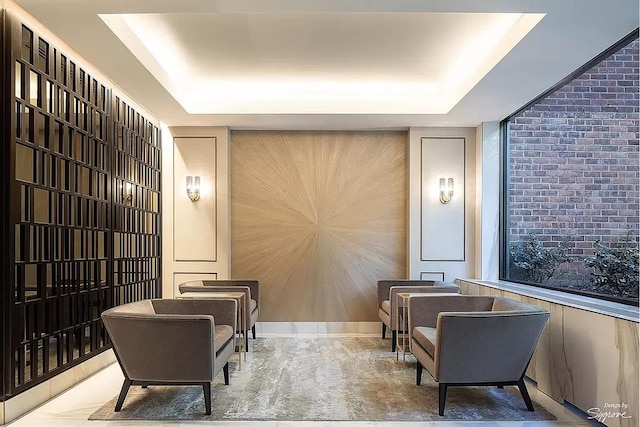 sitting room with a tray ceiling, an accent wall, and brick wall