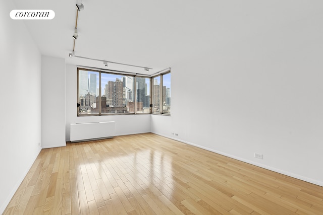 spare room featuring radiator, track lighting, wood finished floors, a skyline view, and baseboards