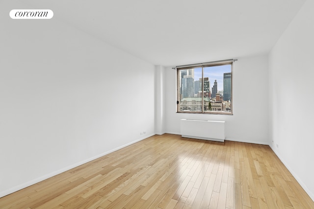 empty room with radiator heating unit, wood finished floors, baseboards, and a city view