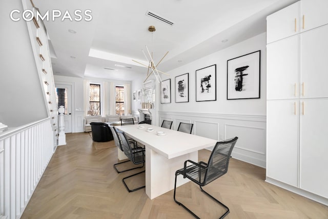 dining space featuring visible vents, a decorative wall, a tray ceiling, and a wainscoted wall