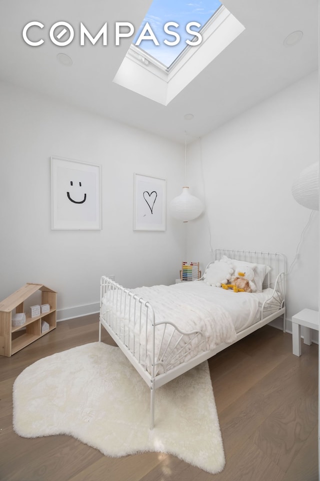 bedroom featuring baseboards, wood finished floors, and a skylight