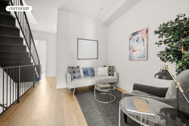 living area with baseboards, wood finished floors, and stairway