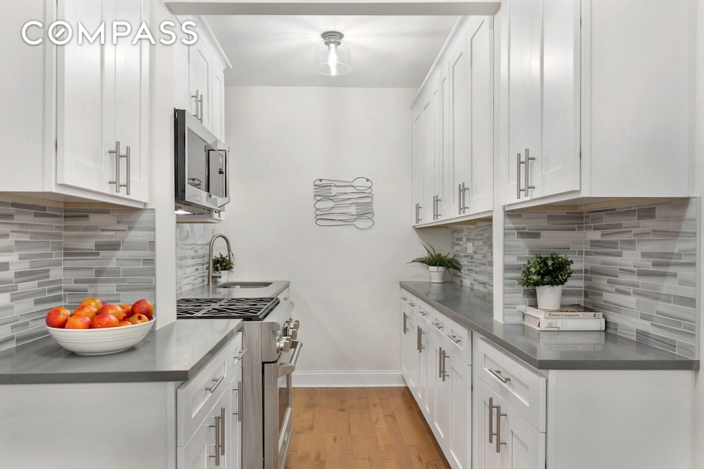 345 Riverside Dr Unit 1E, New York City, NY 10025 - kitchen featuring appliances with stainless steel finishes, decorative backsplash, light wood-style floors, and white cabinets