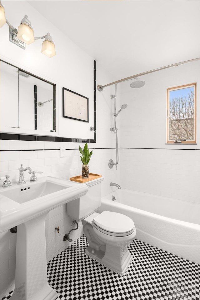 full bath featuring toilet, a sink,  shower combination, and tile walls