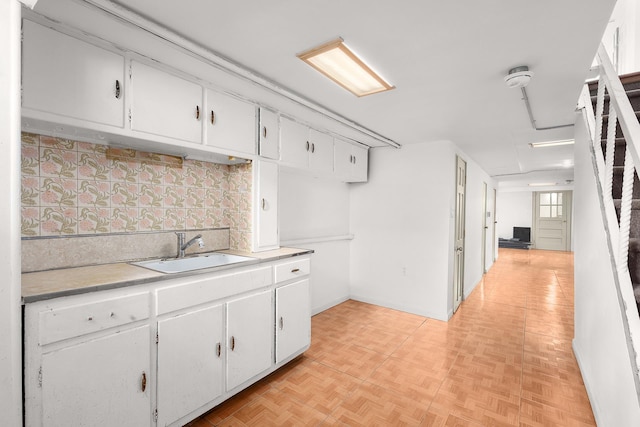 kitchen featuring white cabinets, light countertops, a sink, and backsplash