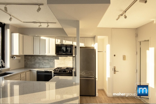 kitchen with rail lighting, appliances with stainless steel finishes, a sink, decorative backsplash, and light wood-style flooring