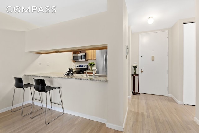 350 W 50th St Unit 3Ll, New York City, NY 10019 - kitchen featuring appliances with stainless steel finishes, light wood-style flooring, tasteful backsplash, baseboards, and a peninsula