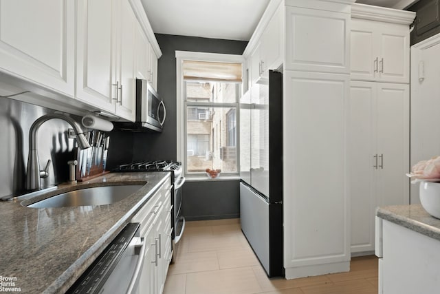 kitchen featuring a sink, appliances with stainless steel finishes, dark stone counters, and white cabinetry