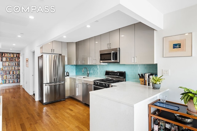 kitchen with stainless steel appliances, gray cabinetry, a peninsula, light countertops, and light wood-style floors