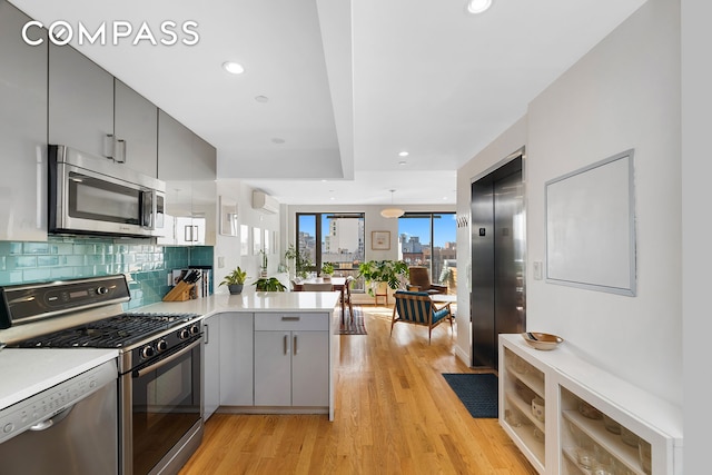 kitchen featuring appliances with stainless steel finishes, a peninsula, elevator, gray cabinetry, and light wood finished floors