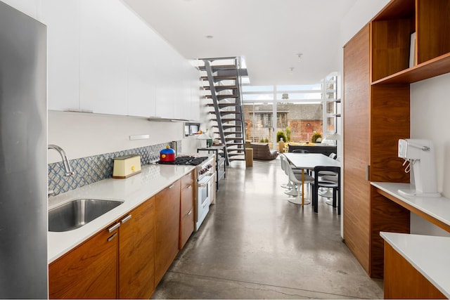 kitchen featuring range with gas cooktop, a sink, modern cabinets, backsplash, and brown cabinets
