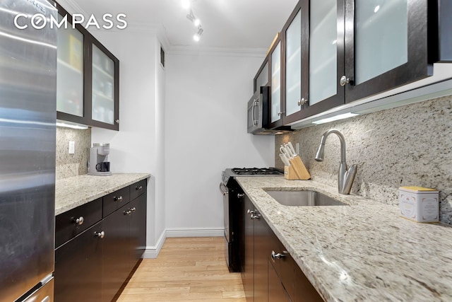 kitchen with a sink, light wood-style floors, stainless steel appliances, ornamental molding, and glass insert cabinets