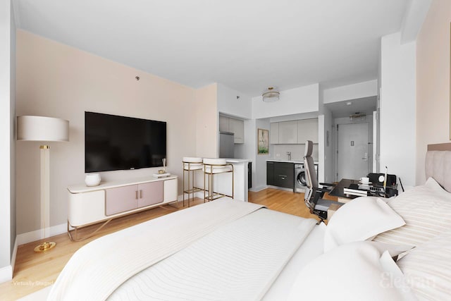 bedroom with washer / dryer, light wood-style floors, refrigerator, and baseboards