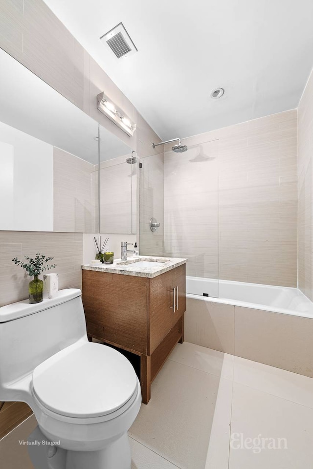bathroom featuring toilet,  shower combination, visible vents, and tile walls