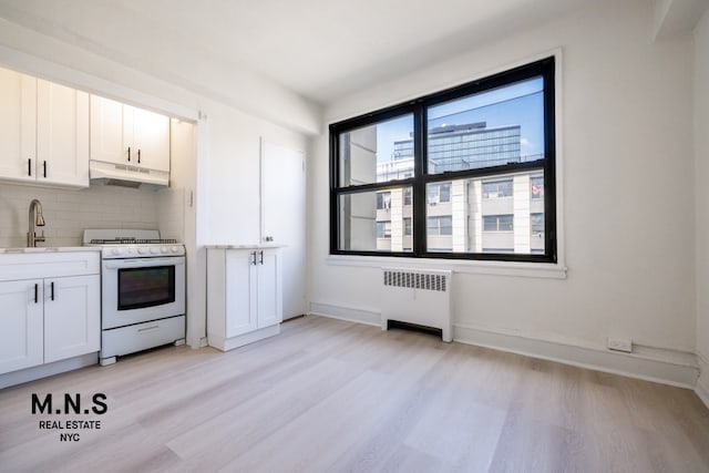 98-19 64th Ave Unit 6-Gg, New York City, NY 11374 - kitchen with radiator, white gas stove, under cabinet range hood, and light wood finished floors