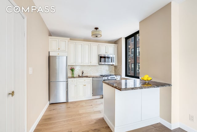 kitchen featuring appliances with stainless steel finishes, decorative backsplash, dark stone countertops, light wood-style floors, and baseboards