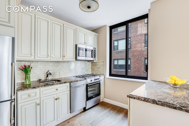 kitchen with stainless steel appliances, a sink, light wood-style floors, backsplash, and baseboards