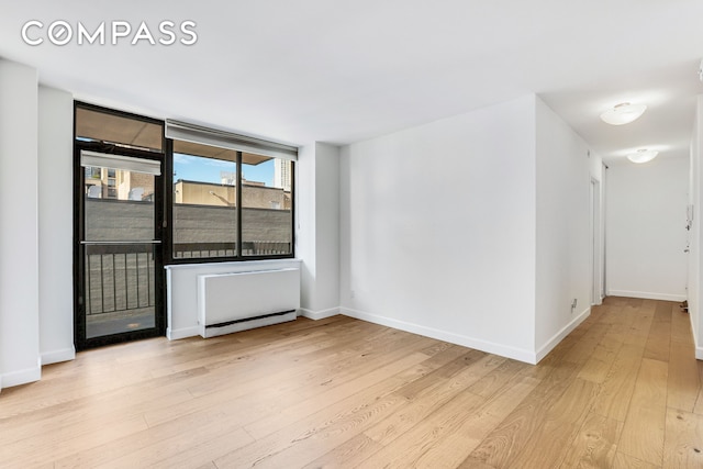 empty room with wood finished floors, a baseboard radiator, and baseboards