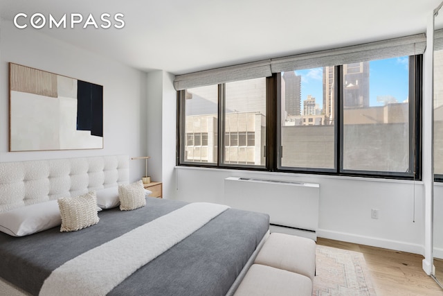 bedroom with wood finished floors, radiator, baseboards, and a city view