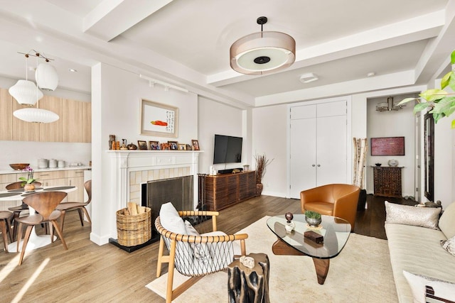 living room with light wood finished floors, a tile fireplace, and beamed ceiling