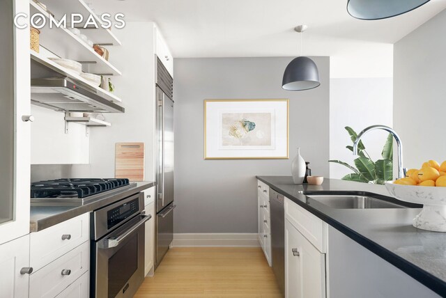 kitchen with open shelves, dark countertops, appliances with stainless steel finishes, light wood finished floors, and a sink