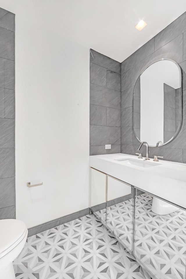 bathroom with toilet, tile patterned floors, tile walls, and a sink