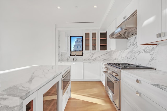 kitchen with backsplash, light stone counters, stainless steel range, under cabinet range hood, and white cabinetry