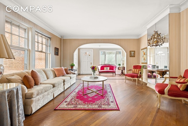 living room featuring hardwood / wood-style floors, arched walkways, an inviting chandelier, and ornamental molding