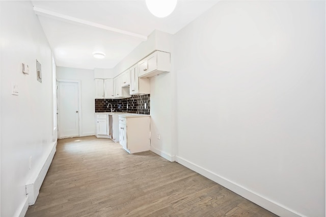 309 Covert St, New York City, NY 11237 - kitchen featuring decorative backsplash, light wood-style floors, white cabinets, and baseboards