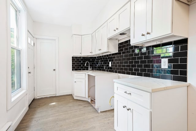 309 Covert St, New York City, NY 11237 - kitchen with a sink, light wood-style flooring, decorative backsplash, white cabinets, and a baseboard heating unit