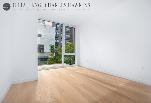 spare room featuring baseboards, wood finished floors, and a wall of windows