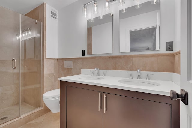 bathroom featuring a stall shower, double vanity, toilet, tile walls, and tile patterned flooring