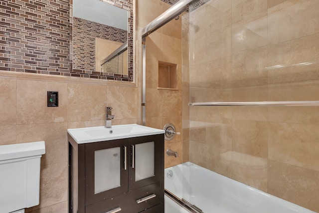 bathroom with tile walls, shower / bath combination with glass door, toilet, and vanity