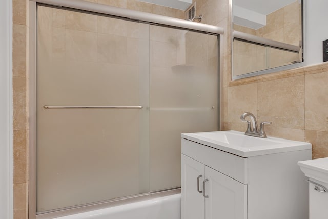 bathroom with tile walls, vanity, toilet, and combined bath / shower with glass door