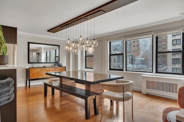 dining room with radiator heating unit, ornamental molding, light wood finished floors, and baseboards