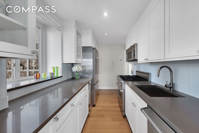 kitchen with white cabinets, a sink, dark countertops, recessed lighting, and high end appliances